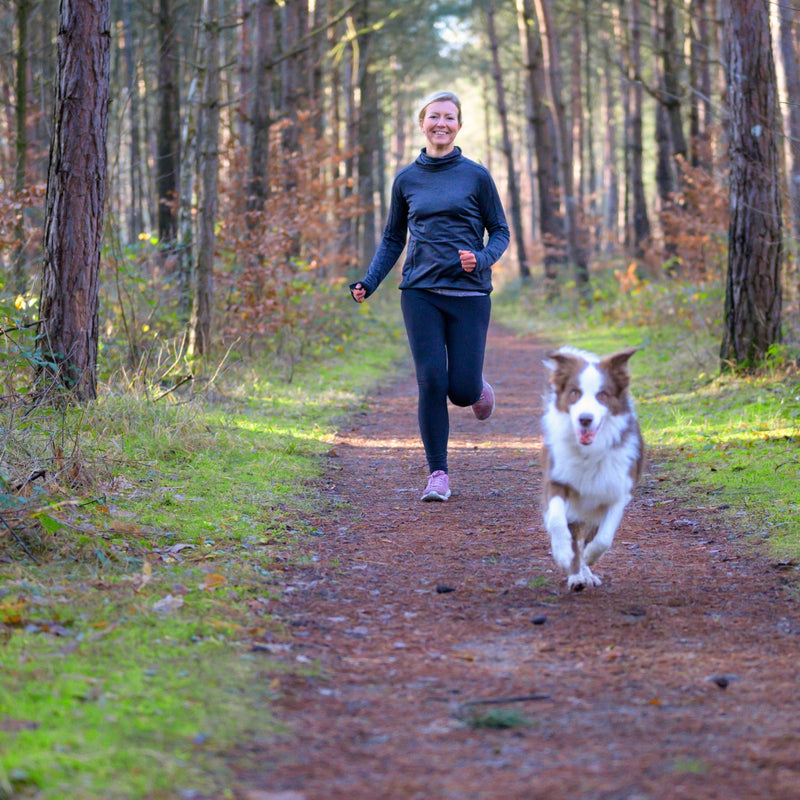 Woman running with a dog on a path in a forest